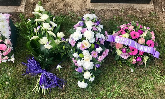 White Flowers in Greenery & Purple Bow, from Loving Great Grandchildren, Matti, Paige and George.