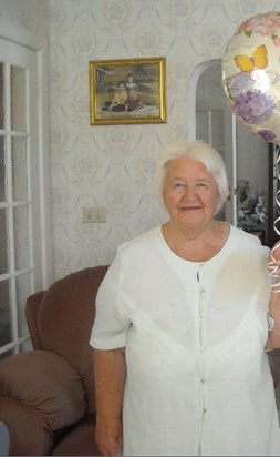 Mum with a photo of her three grandchildren behind her, a few years ago now