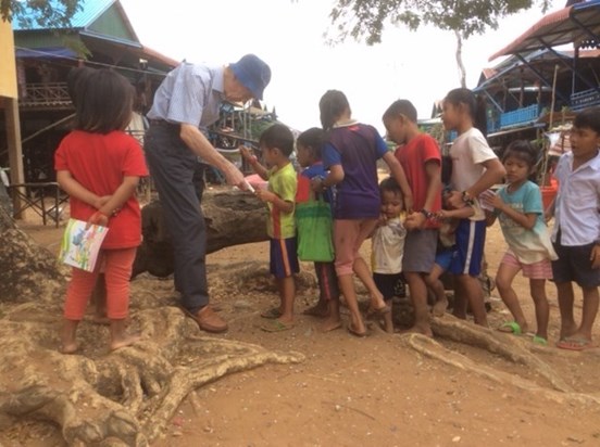 Chris handing out books for the children in the village in Cambodia 