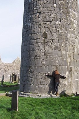 Thelma hugging the leaning round tower of Kilmacdaugh, Ireland, February 2006